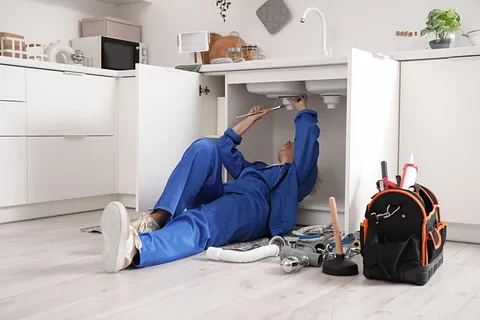 Mogen kvinnlig rörmokare som installerar handfat i köket