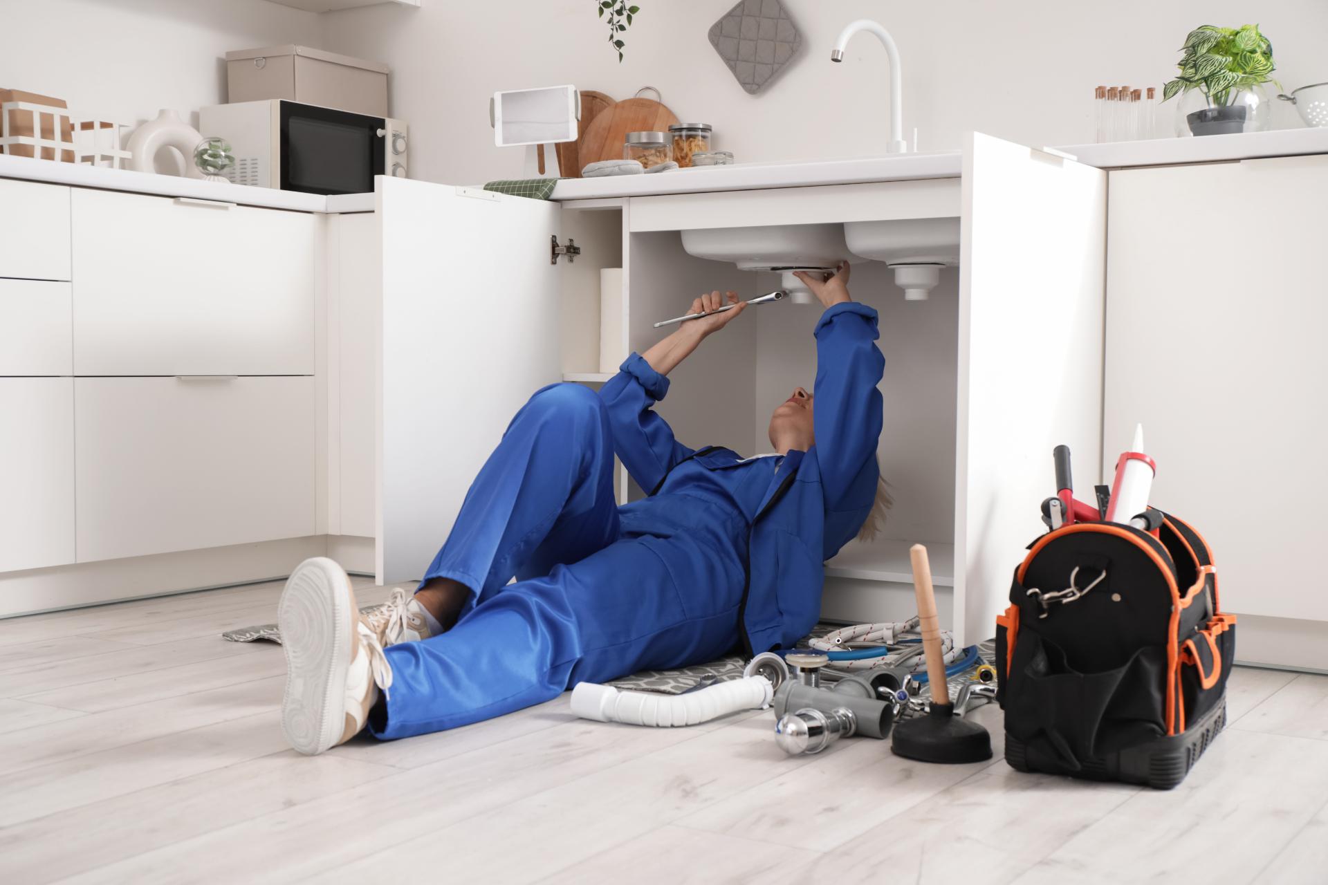 Mogen kvinnlig rörmokare som installerar handfat i köket